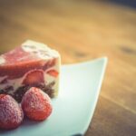 Une délicieuse part de gâteau à la crème de fraise avec des fraises fraîches sur une assiette moderne blanche.