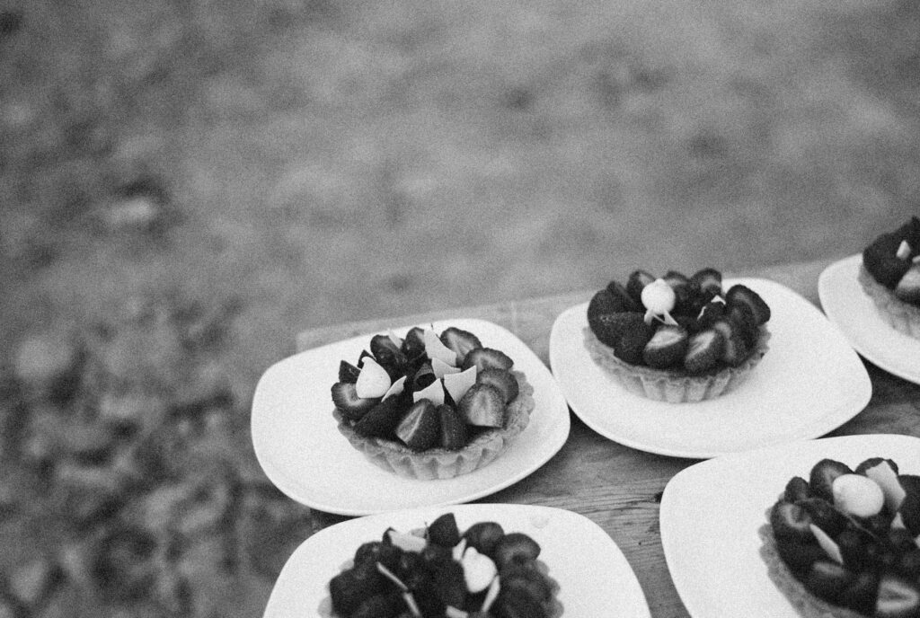 Gros plan sur des tartelettes aux fraises sur des assiettes en céramique en noir et blanc, créant une ambiance classique et artistique.