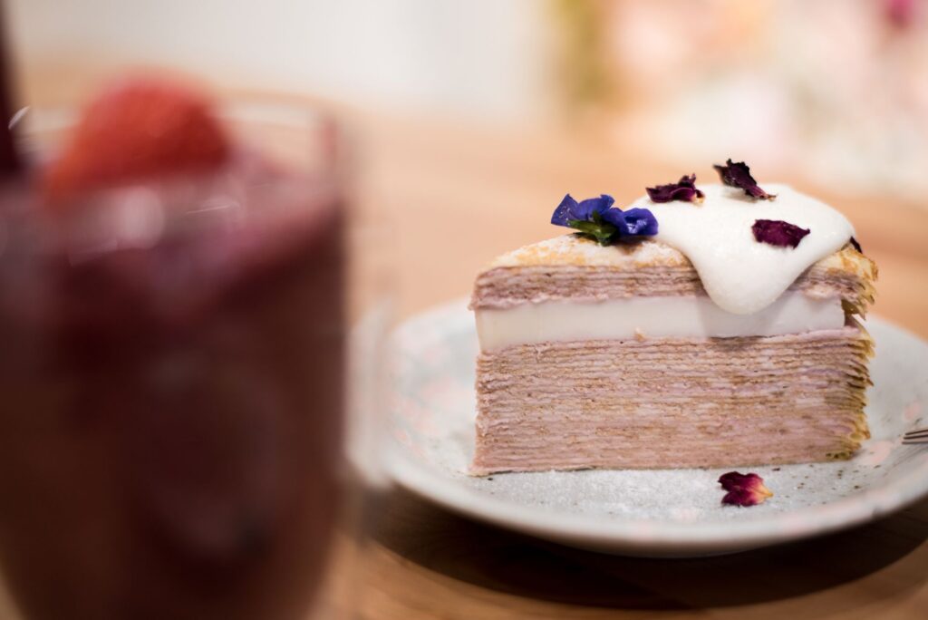 Tranche de gâteau en couches de crêpes avec garniture de crème et décoration florale sur une assiette à l'intérieur.