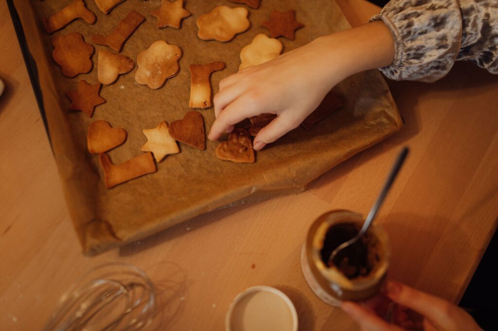 Vue rapprochée de mains décorant des biscuits en forme d'étoile et de nuage sur du papier sulfurisé.