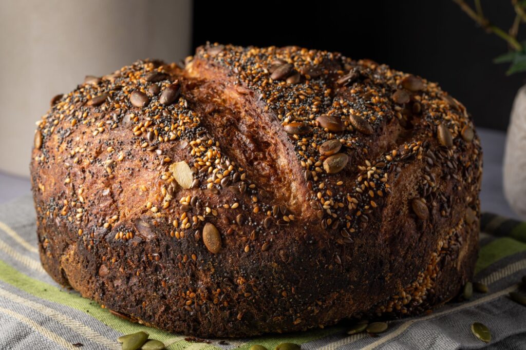Gros plan sur une miche de pain artisanal fait maison garnie de graines de citrouille et de sésame.