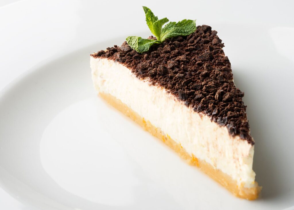 Une délicieuse part de cheesecake garnie de chocolat et de menthe sur une assiette blanche.