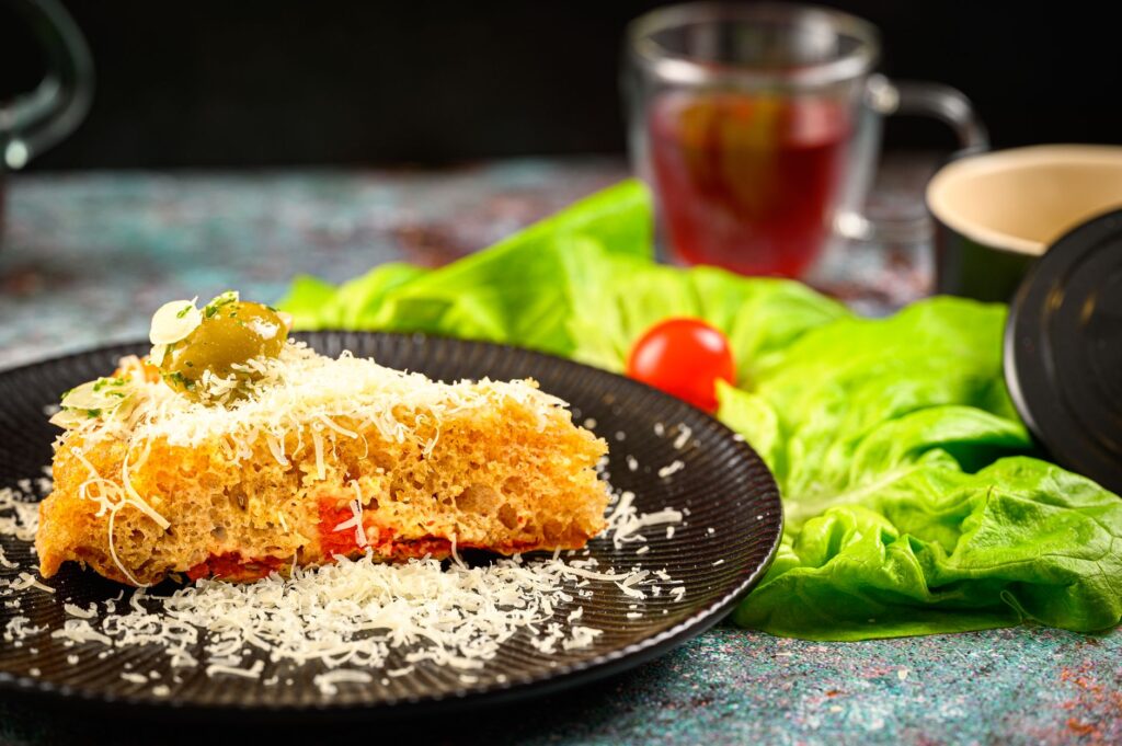 Une tranche de pain gourmet garnie de fromage et d'olive, entourée de laitue fraîche et de tomate.