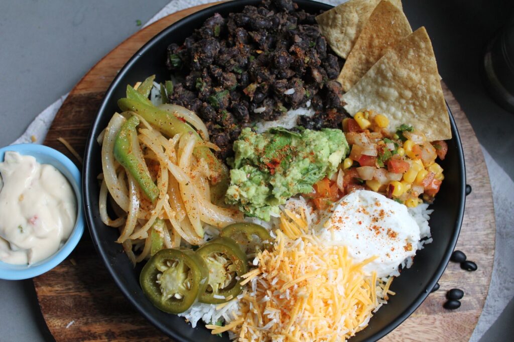 Bol burrito mexicain coloré avec du guacamole, des haricots noirs et du fromage râpé.