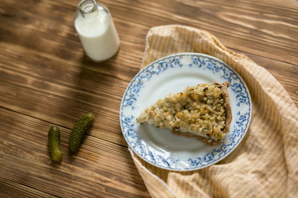 Part de tarte savoureuse sur une assiette décorative avec du lait et des cornichons.
