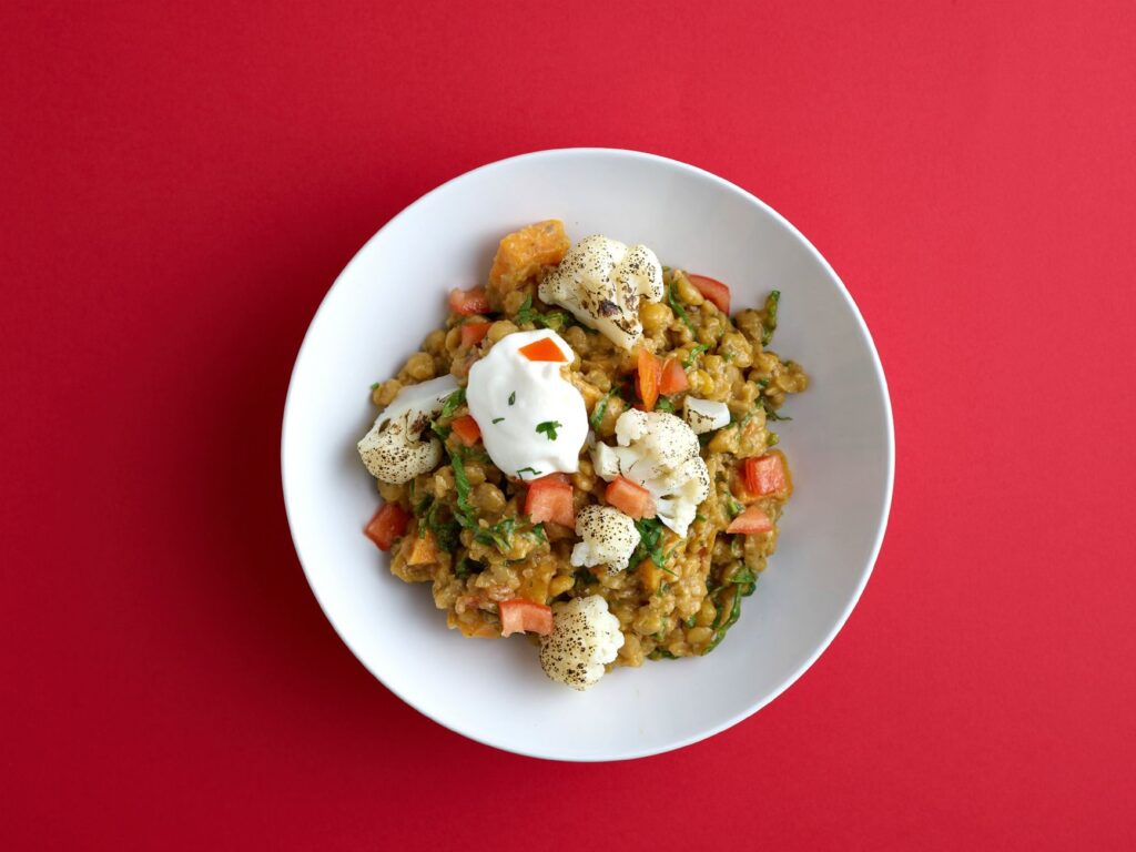 Délicieux curry de légumes avec chou-fleur et épices dans un bol blanc sur un fond rouge.