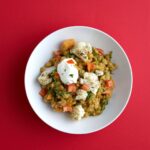 Délicieux curry de légumes avec chou-fleur et épices dans un bol blanc sur un fond rouge.