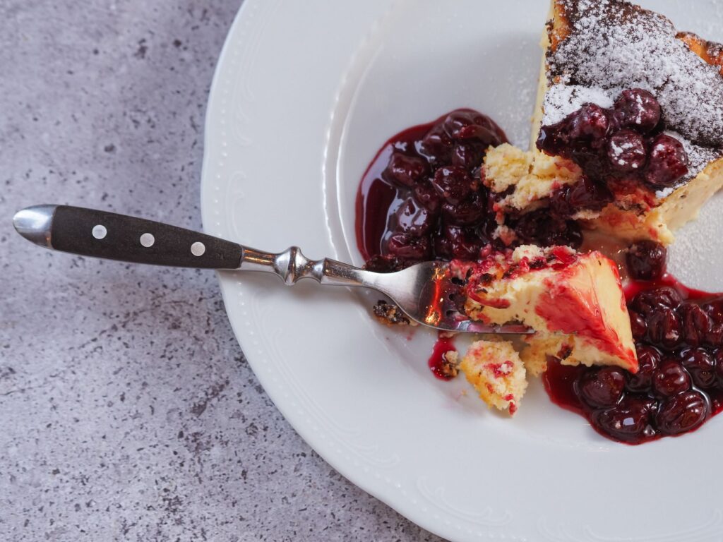 Délicieuse part de cheesecake garnie de cerises et de sucre glace sur une assiette blanche.
