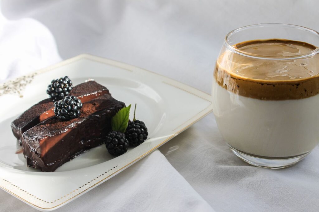 Gâteau au chocolat orné de mûres accompagné d'un café Dalgona crémeux, capturé dans un cadre lumineux et accueillant.