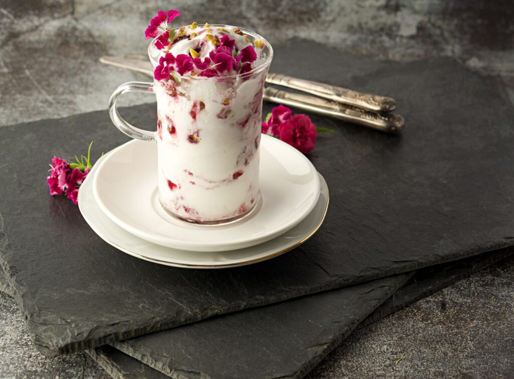 Délicieux dessert au yaourt garni de fleurs comestibles, servi sur des assiettes en schiste pour une touche gourmet.