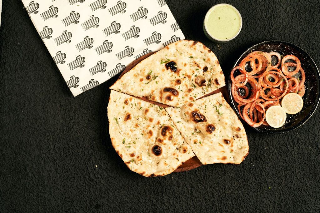 Délicieux naan cuit au four servi avec une salade d’oignons acidulée et un chutney vert, parfait pour les amateurs de cuisine indienne.