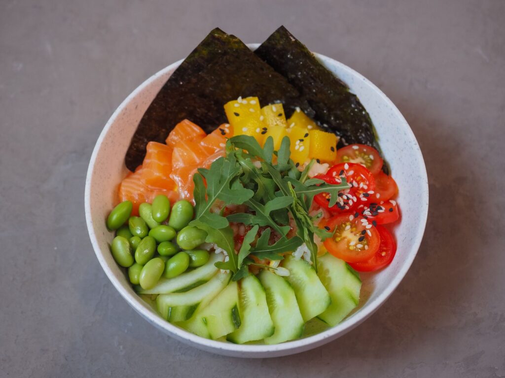 Gros plan sur un poke bowl vibrant avec des légumes frais, du saumon et des algues sur un fond neutre.