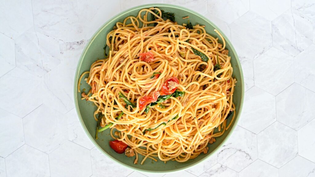 Des spaghettis appétissants avec des épinards et des tomates sur une assiette en céramique verte.