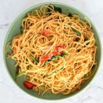 Des spaghettis appétissants avec des épinards et des tomates sur une assiette en céramique verte.
