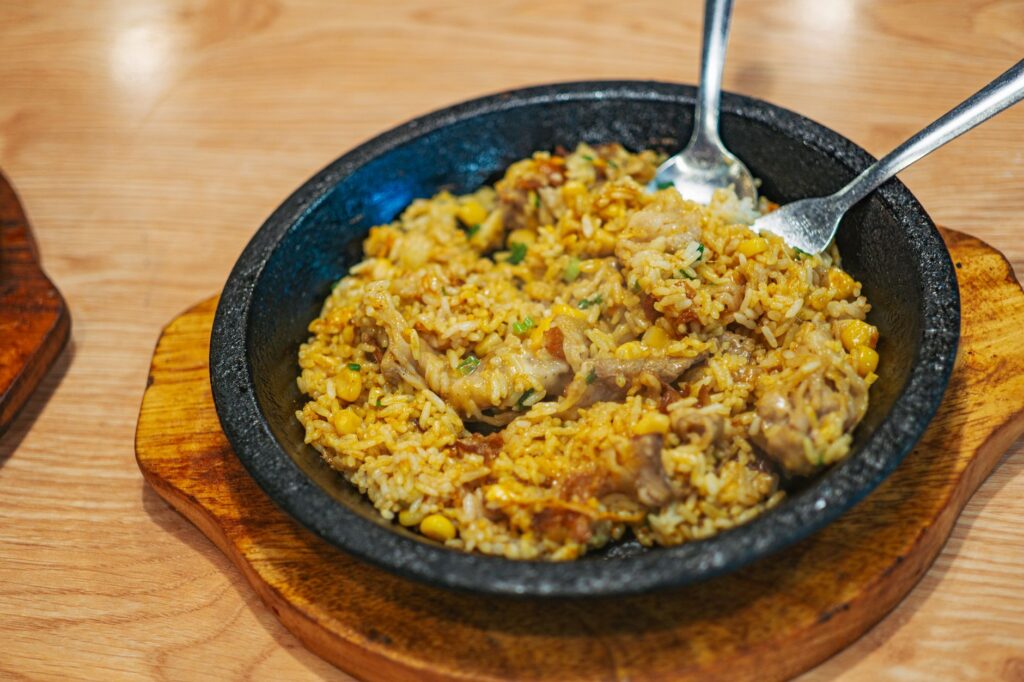 Riz frit crépitant avec du maïs et de la viande servi chaud dans une poêle en fonte.