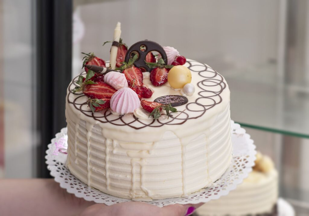 Gros plan d'un gâteau à la crème vanille magnifiquement décoré, surmonté de fraises fraîches et de détails en chocolat élégants.