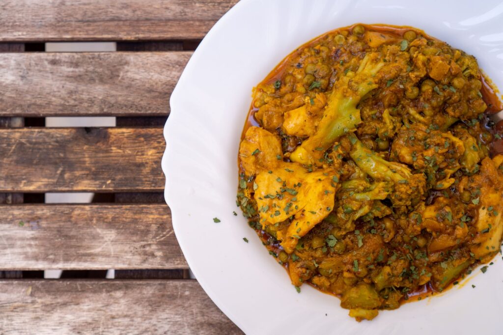 Gros plan sur un curry indien épicé avec des légumes servi dans une assiette blanche sur une table en bois rustique.
