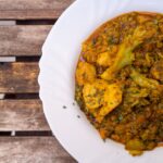 Gros plan sur un curry indien épicé avec des légumes servi dans une assiette blanche sur une table en bois rustique.