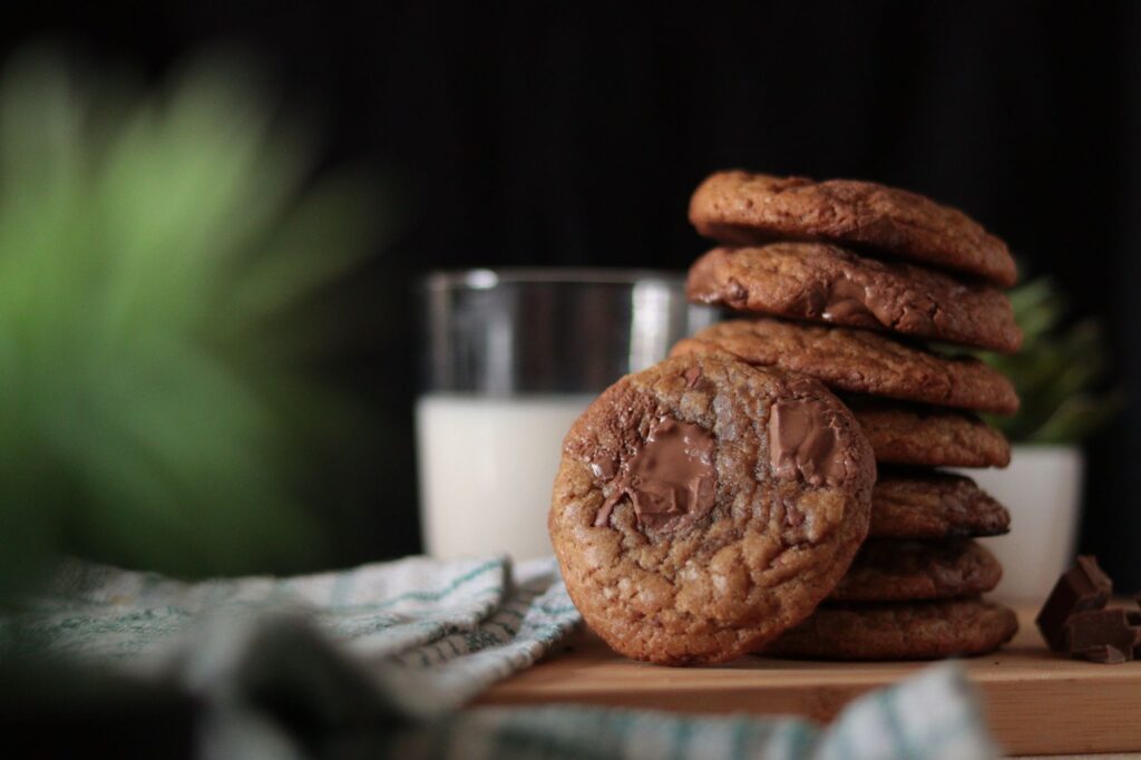 Gros plan de cookies aux pépites de chocolat empilés à côté d'un verre de lait, mettant en avant leur nature sucrée et gourmande.