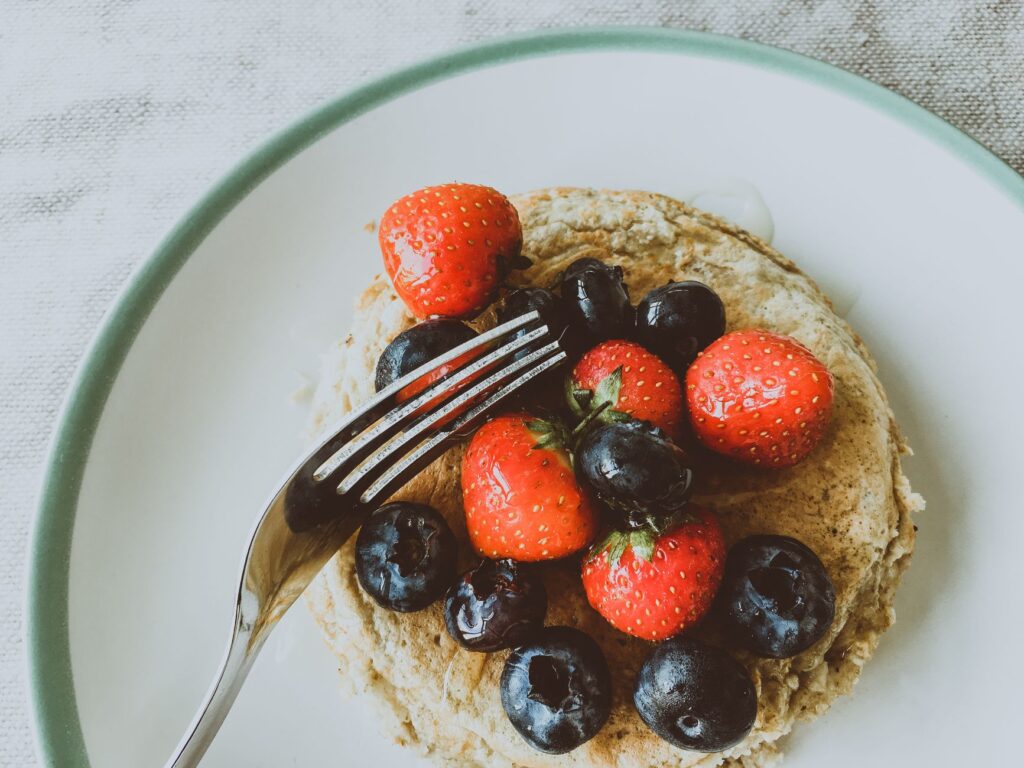 Pile de pancakes garnie de fraises et de myrtilles fraîches sur une assiette.