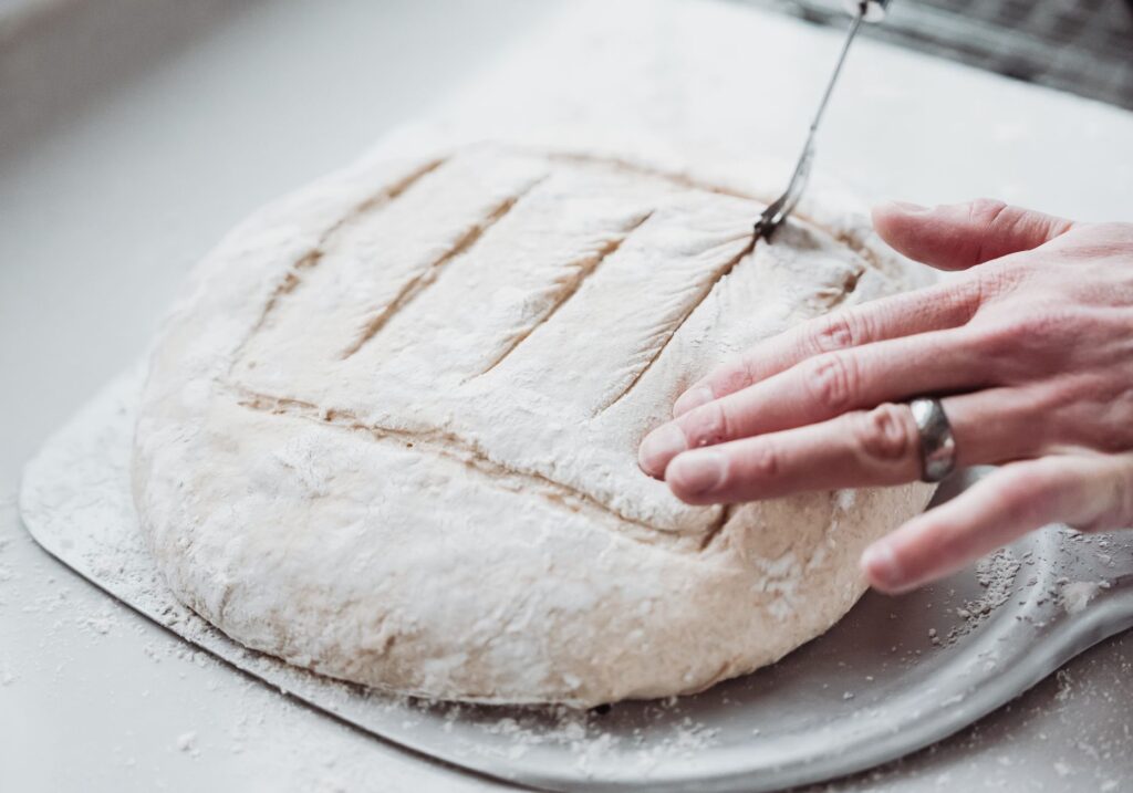 Une vue détaillée des mains marquant la pâte à pain pour la cuisson, mettant en valeur la préparation artisanale du pain.