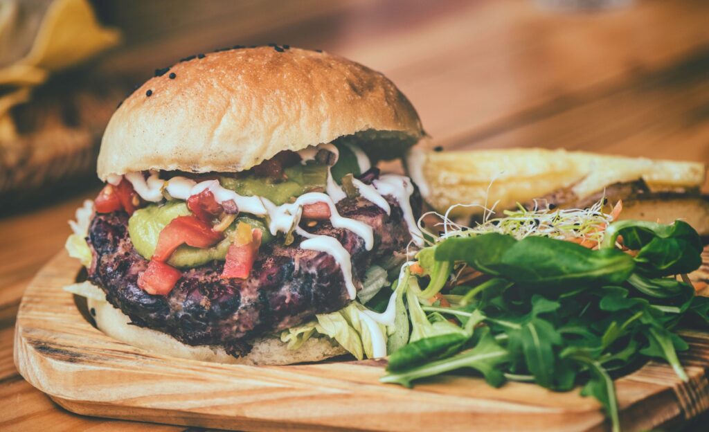 Délicieux cheeseburger avec garnitures fraîches et frites sur une planche en bois.