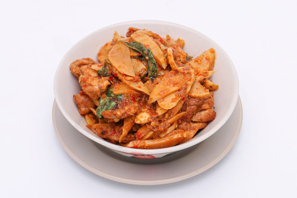 Un plat thaïlandais savoureux de poulet sauté avec des pousses de bambou, du basilic et des épices dans un bol blanc.