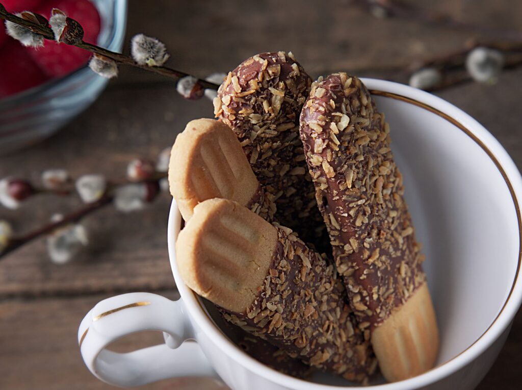 Gros plan sur de délicieux biscuits enrobés de chocolat garnis de noix dans une tasse décorative.