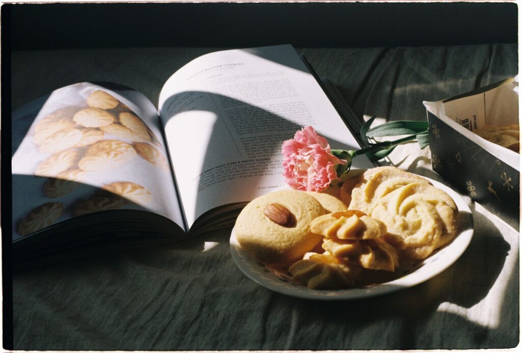 Une scène sereine de biscuits sur une assiette avec un livre de cuisine ouvert et une œillet rose.