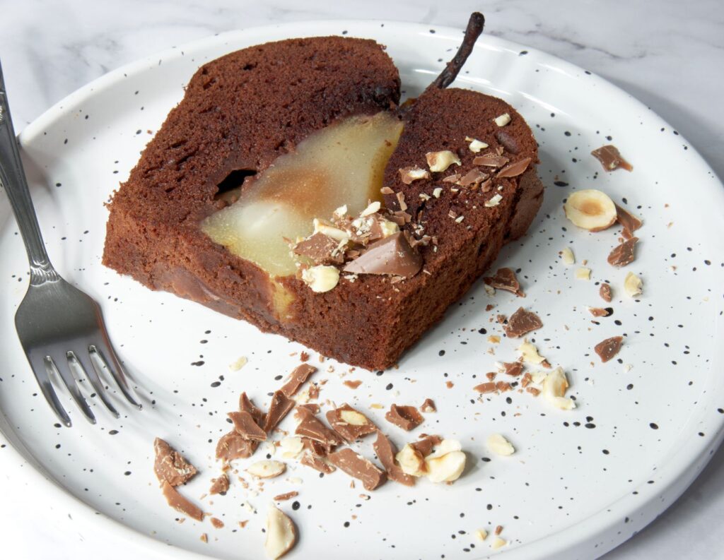 Une part de gâteau au chocolat et poire avec des noisettes sur une assiette tachetée.