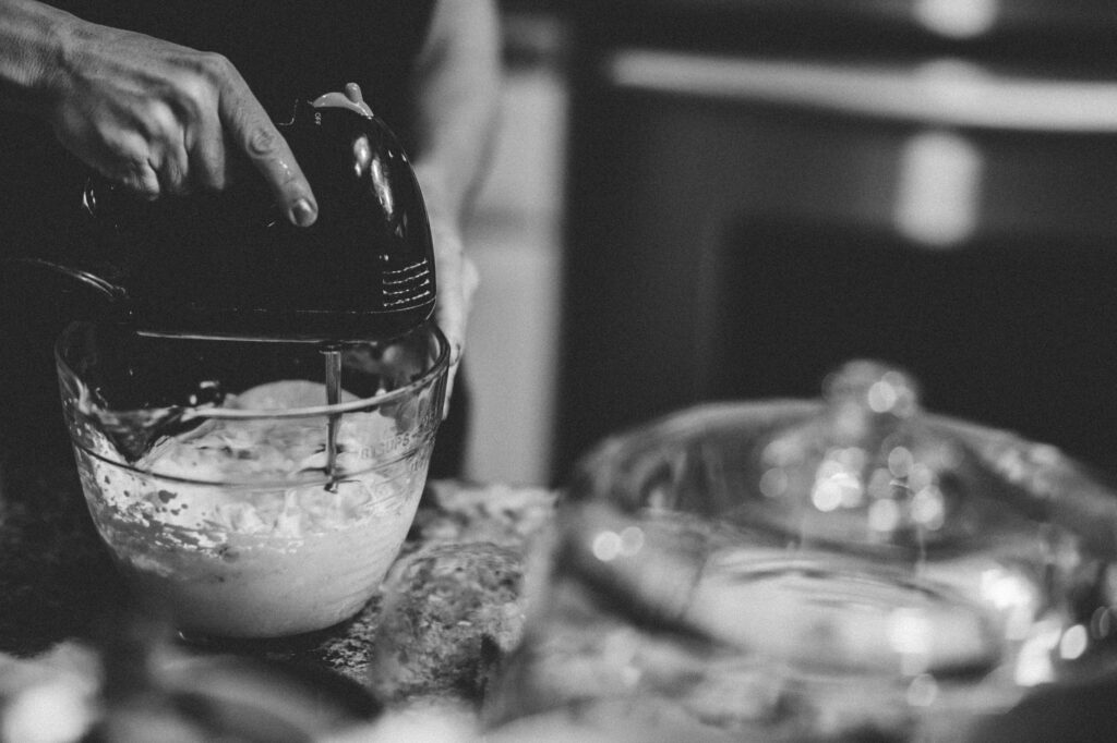 Une main utilisant un batteur électrique dans une cuisine monochrome, créant une scène de pâtisserie classique.