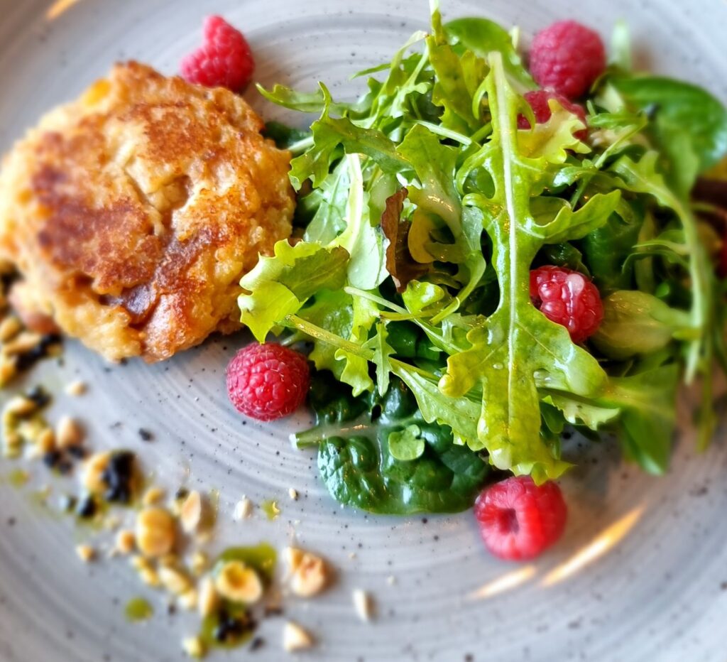 Gros plan d'un repas gourmet mettant en vedette un gâteau de saumon, une salade de roquette fraîche et des framboises.