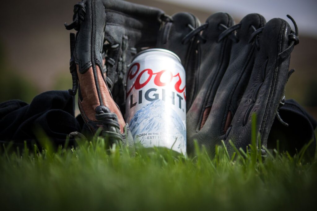 Gros plan d'une canette de Coors Light reposant dans un gant de baseball sur de l'herbe verte fraîche.
