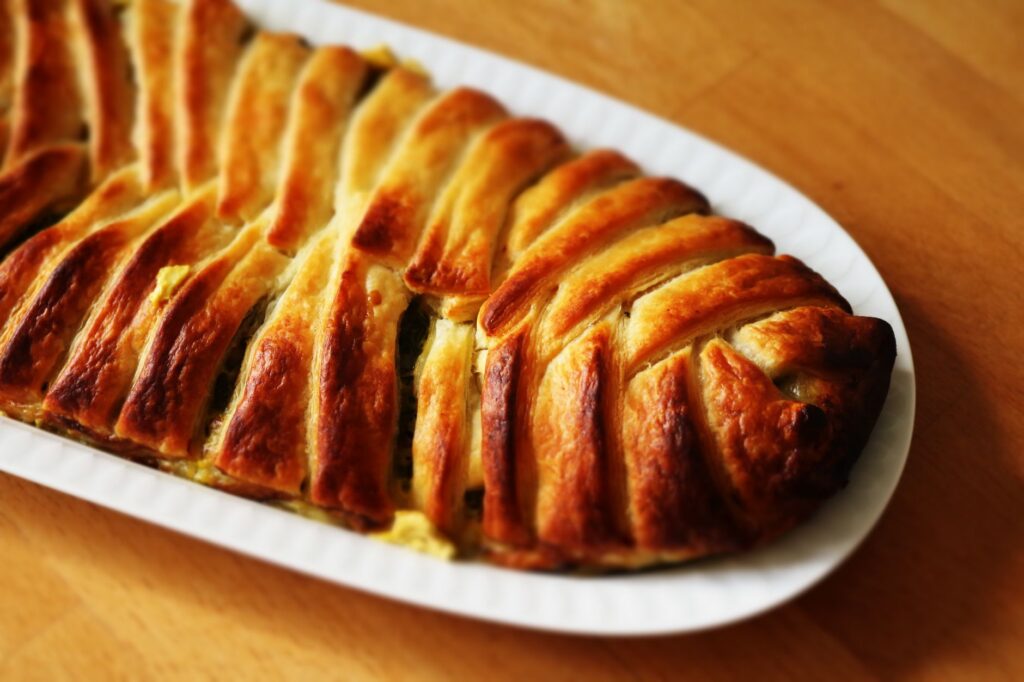 Pâte feuilletée dorée fraîchement cuite avec des couches feuilletées sur une assiette blanche, parfaite pour un repas délicieux.