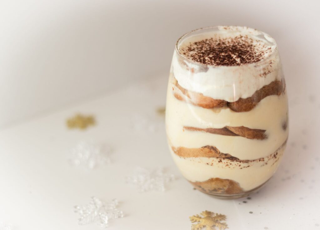 Gros plan sur un dessert tiramisu crémeux dans un verre, joliment présenté avec un topping de cacao, parfait pour une indulgence savoureuse.