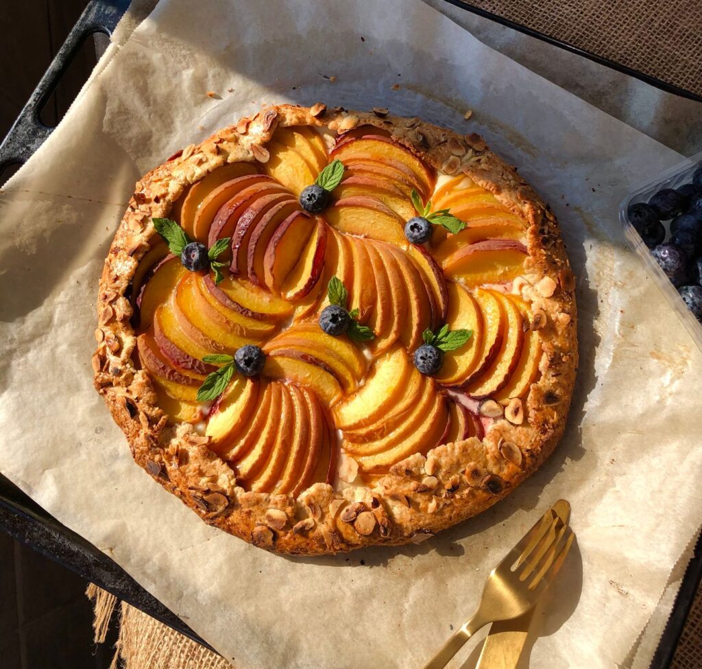 Tarte pêche rustique ensoleillée avec des myrtilles sur papier sulfurisé, parfaite pour les desserts et la photographie culinaire.