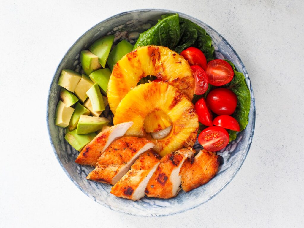 Vue de dessus vibrante d'un bol de salade avec du poulet grillé, de l'ananas, de l'avocat et des tomates cerises.