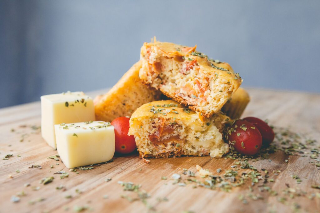 Délicieux muffins au fromage et tomates faits maison avec des herbes, présentés avec des cubes de fromage et des tomates cerises.
