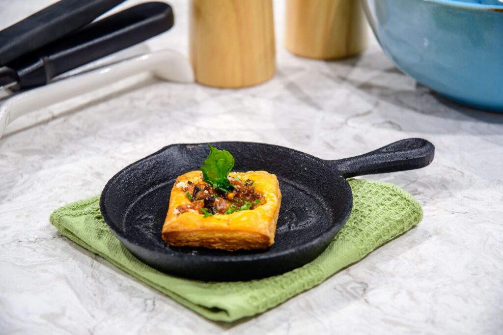 Tarte carrée savoureuse avec du bacon et des garnitures sur une poêle en fonte sur une serviette verte.