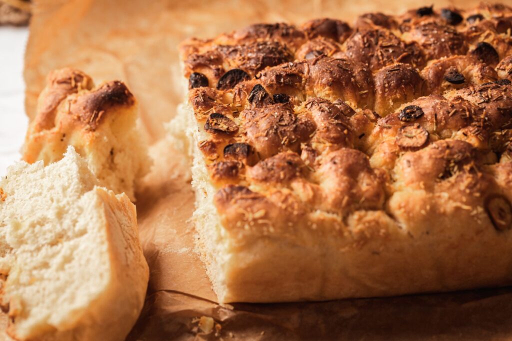 Gros plan de pain focaccia artisanal fraîchement cuit sur du papier sulfurisé, mettant en valeur la texture et la croûte.