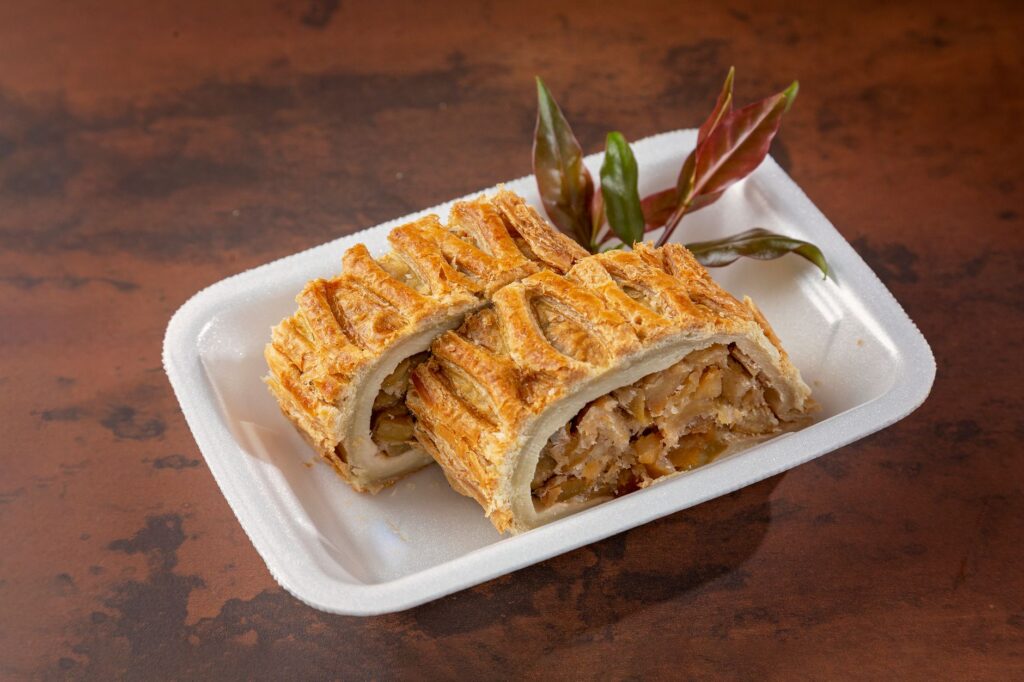 Strudel aux pommes tout juste cuit sur une assiette blanche avec des feuilles décoratives, mettant en valeur sa croustillante dorée.