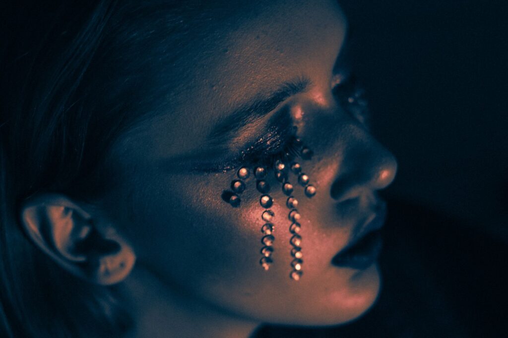 Portrait dramatique d'une femme avec du maquillage pailleté sur un fond sombre.