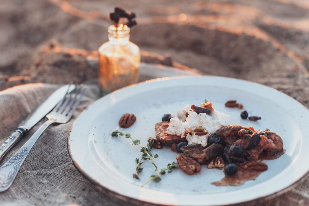 Une scène de dîner en plein air rustique avec une assiette de dessert contenant des noix de pécan et des myrtilles, éclairée par une lumière chaude.