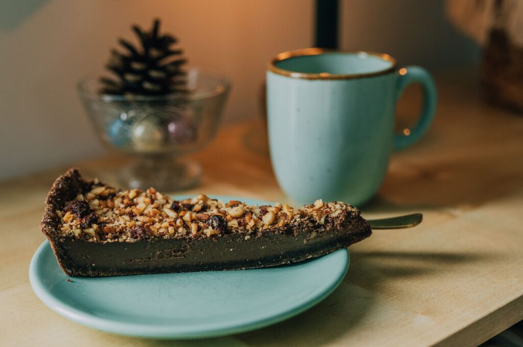 Une tranche de tarte au chocolat et aux noix sur une assiette à côté d'une tasse bleue, parfaite pour une douceur conviviale.