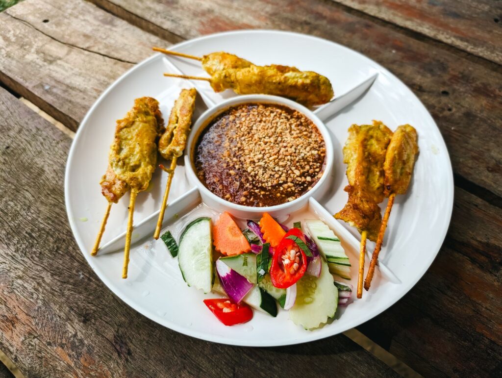 Gros plan sur des brochettes de satay au poulet accompagnées de sauce aux cacahuètes et de légumes frais.