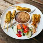 Gros plan sur des brochettes de satay au poulet accompagnées de sauce aux cacahuètes et de légumes frais.