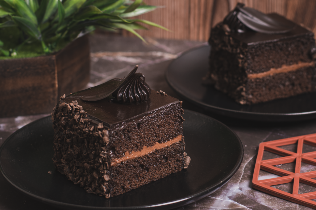 Riches tranches de gâteau au chocolat avec glaçage sur des assiettes noires, parfaites pour les desserts et la photographie culinaire.