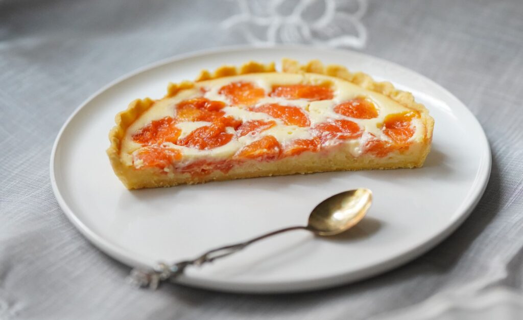 Gros plan d'une tranche de tarte aux abricots fraîchement cuite servie sur une assiette blanche.