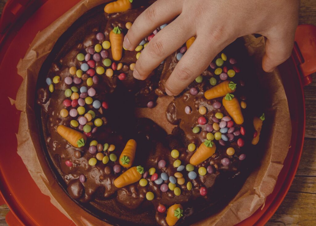 Un gros plan d'un gâteau au chocolat décoré de bonbons et de carottes, touché par une main.