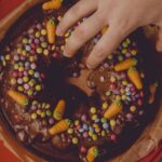 Un gros plan d'un gâteau au chocolat décoré de bonbons et de carottes, touché par une main.
